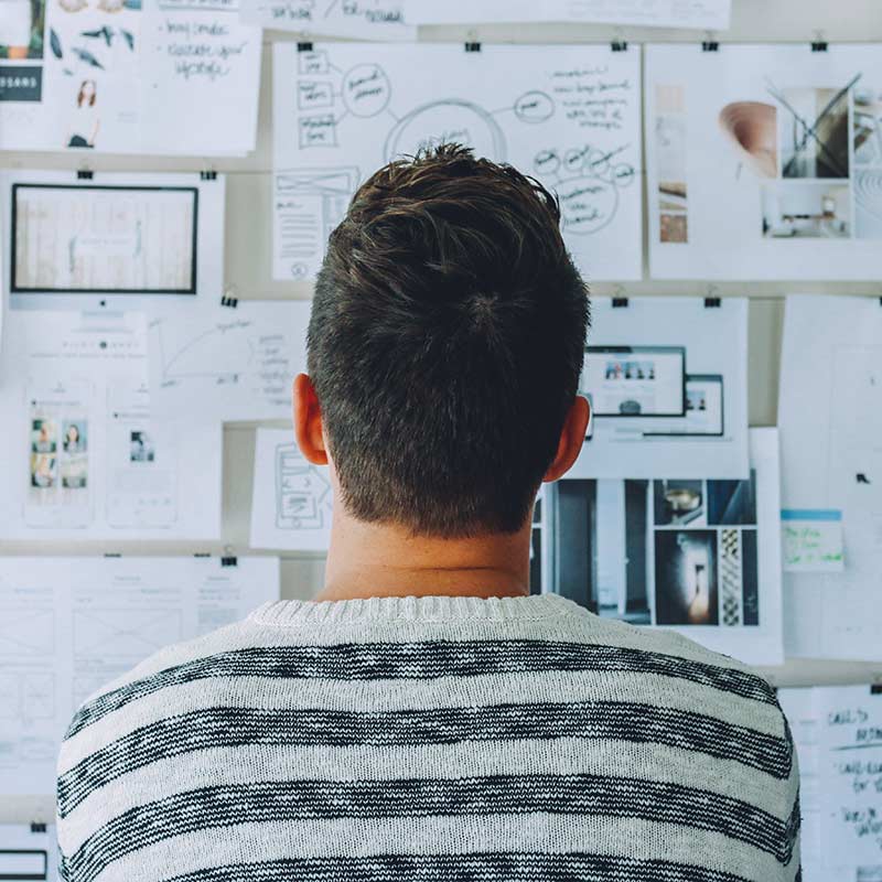 Hombre en una camiseta de rayas blancas y negras mirando una pared de notas y gráficos